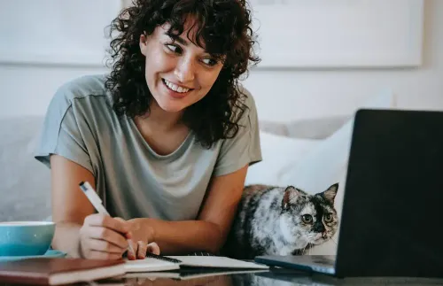 crop_young_positive_female_smiling_and_taking_notes_in_organizer_while_cat_watching_on_netbook_at_table_at_home.webp