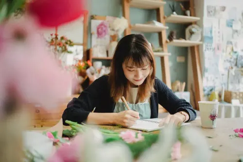 glad_asian_florist_writing_in_notebook_in_flower_shop.webp