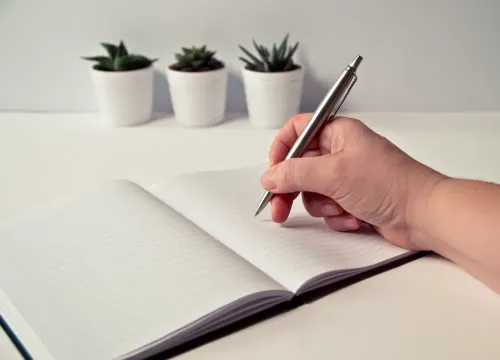 person_holding_silver_retractable_pen_in_white_ruled_book.webp