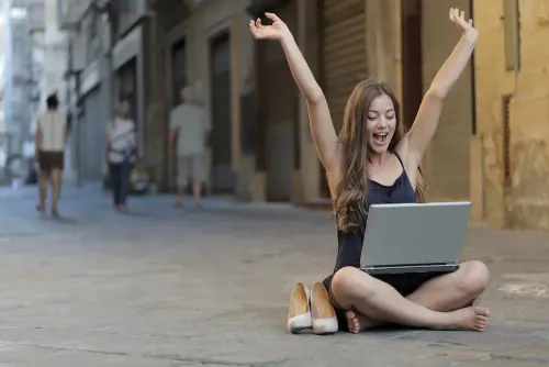 woman_raising_her_hands_up_while_sitting_on_floor_with_macbook_pro_on_lap.webp