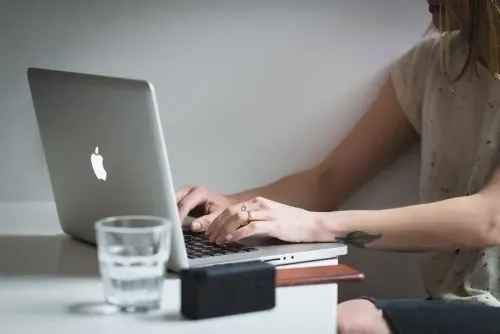 woman_using_silver_macbook_near_shot_glass_on_table.webp